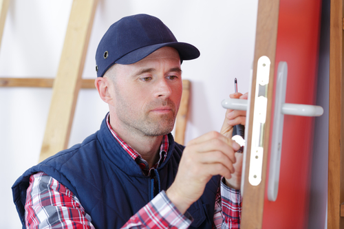 carpenter with doorlock during lock process installation into wood door